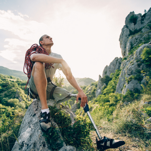 man with prosthetic leg sitting on a rock with climbing gear